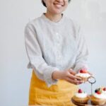 Smiling baker with cupcakes in a cozy kitchen setting.